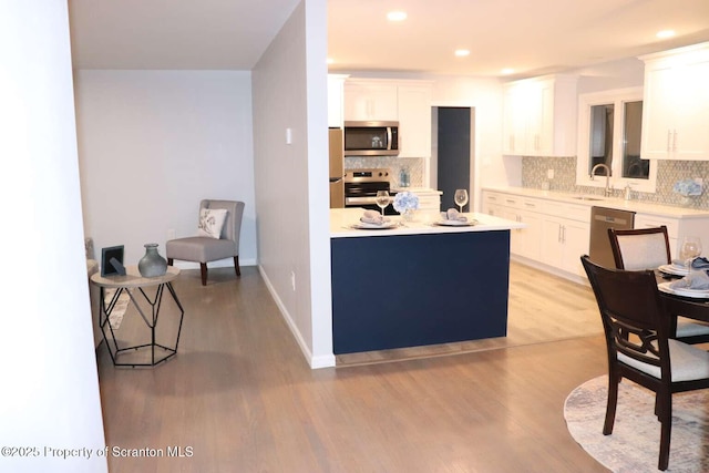 kitchen with white cabinetry, stainless steel appliances, light hardwood / wood-style flooring, and backsplash