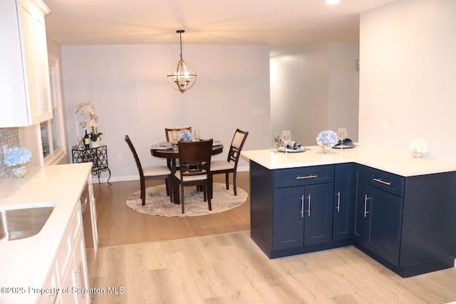 kitchen with blue cabinetry, an inviting chandelier, white cabinetry, light hardwood / wood-style floors, and decorative light fixtures