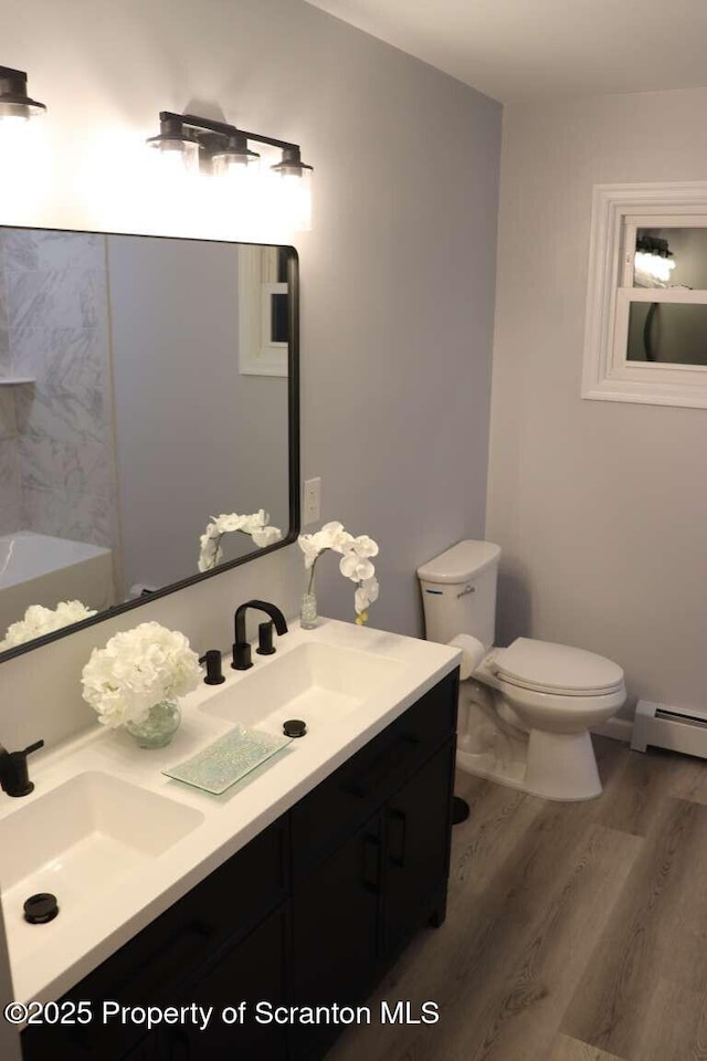 bathroom featuring wood-type flooring, vanity, baseboard heating, and toilet