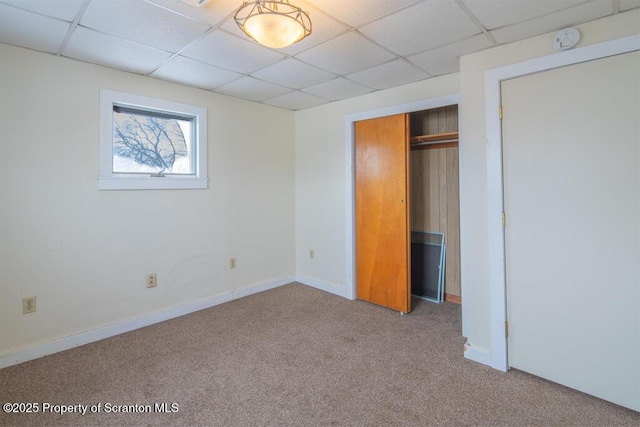 unfurnished bedroom featuring carpet, a closet, a drop ceiling, and baseboards