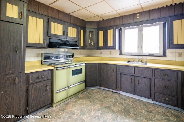 kitchen with stone finish flooring, under cabinet range hood, a drop ceiling, double oven range, and a sink