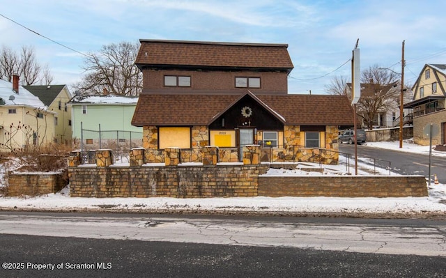 front of property with fence, stone siding, and roof with shingles