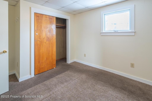 unfurnished bedroom with carpet flooring, baseboards, a closet, and a drop ceiling