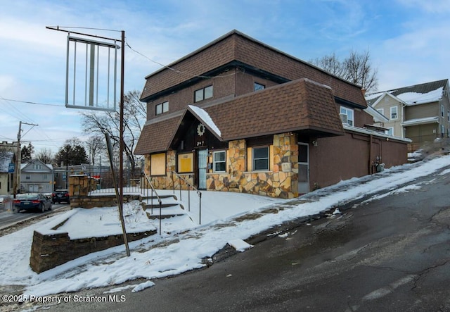 view of front of home with stucco siding, mansard roof, stone siding, and a shingled roof