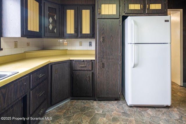 kitchen with stone finish flooring, tasteful backsplash, light countertops, and freestanding refrigerator