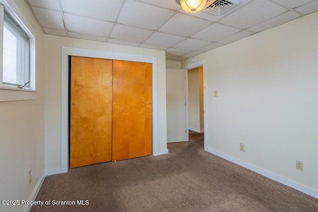 unfurnished bedroom featuring baseboards, visible vents, a drop ceiling, a closet, and carpet flooring