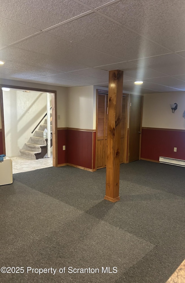 finished below grade area featuring wainscoting, stairway, baseboard heating, carpet flooring, and wood walls