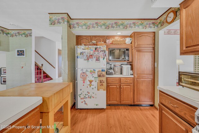 kitchen with brown cabinetry, light wood-type flooring, light countertops, and freestanding refrigerator