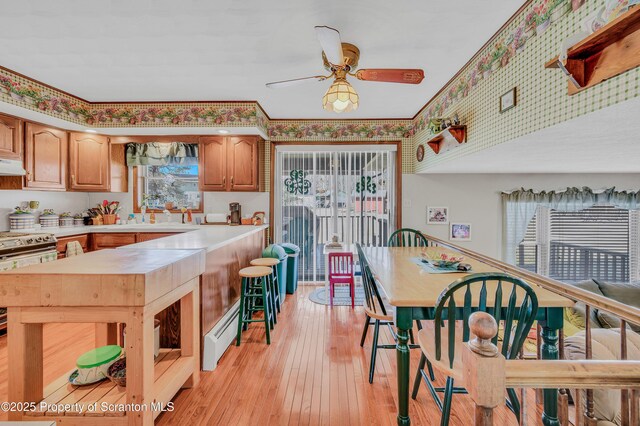 kitchen with light wood finished floors, wallpapered walls, light countertops, under cabinet range hood, and a baseboard heating unit