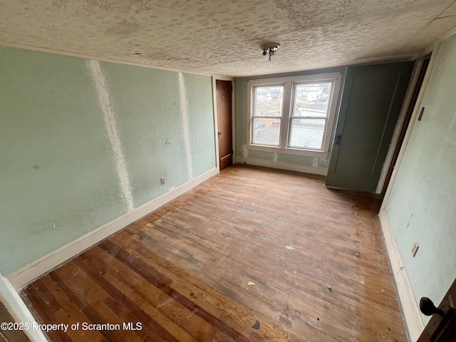 unfurnished room featuring baseboards, a textured ceiling, and hardwood / wood-style floors