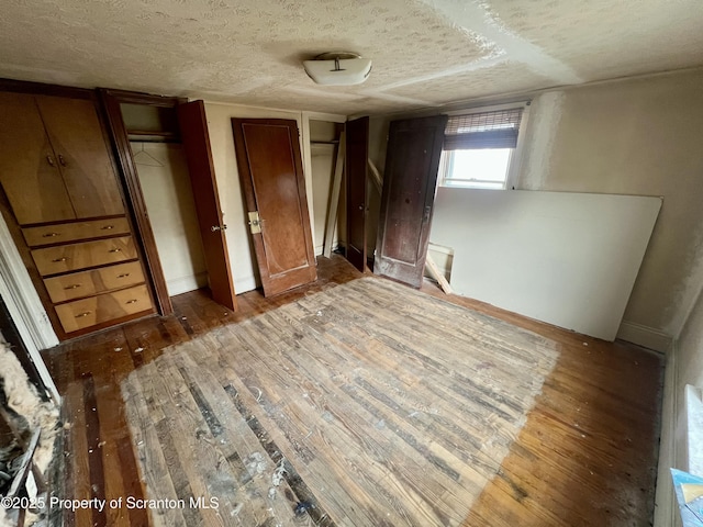 unfurnished bedroom with baseboards, a textured ceiling, multiple closets, and hardwood / wood-style flooring