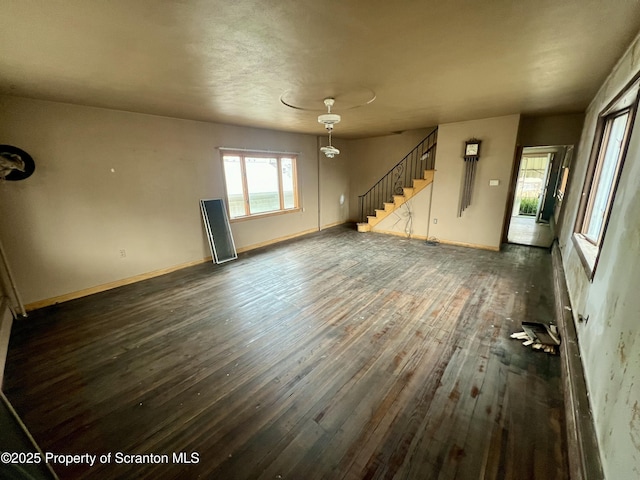 unfurnished living room featuring baseboards, dark wood-style floors, and stairs