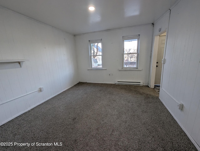 empty room featuring dark colored carpet, crown molding, wood walls, and a baseboard heating unit