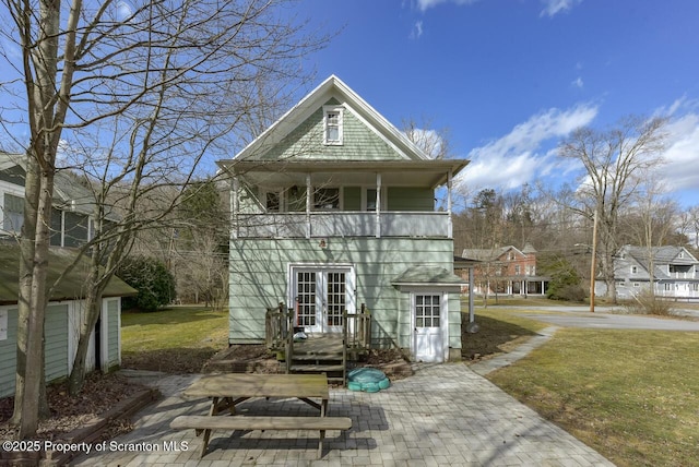 rear view of property with french doors, a lawn, and a balcony