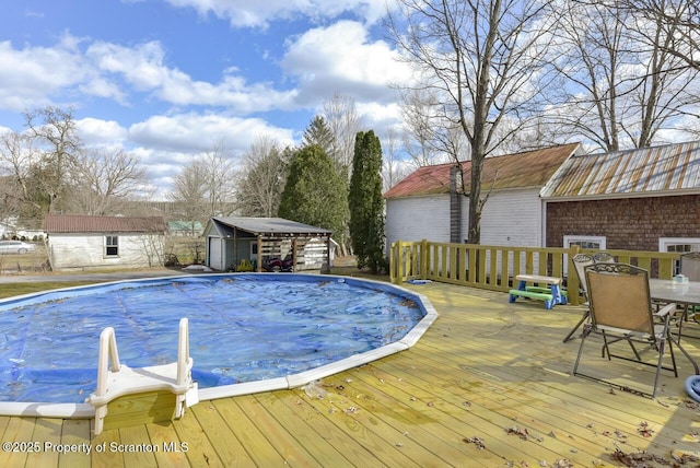 view of pool with a covered pool, a wooden deck, outdoor dining area, a storage shed, and an outbuilding