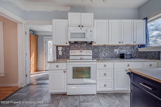 kitchen with white appliances, white cabinets, light tile patterned flooring, and backsplash