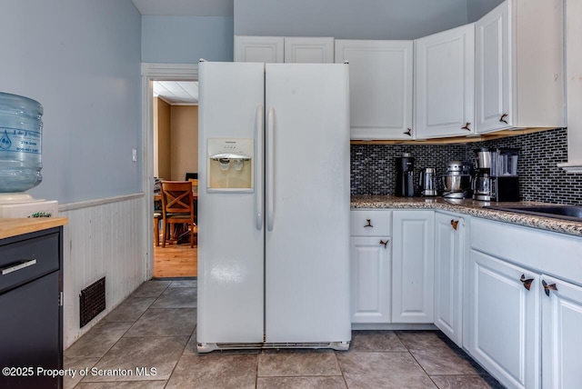 kitchen with white cabinets, white refrigerator with ice dispenser, light tile patterned flooring, and a wainscoted wall