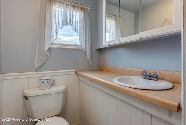 half bath featuring wainscoting, toilet, and vanity