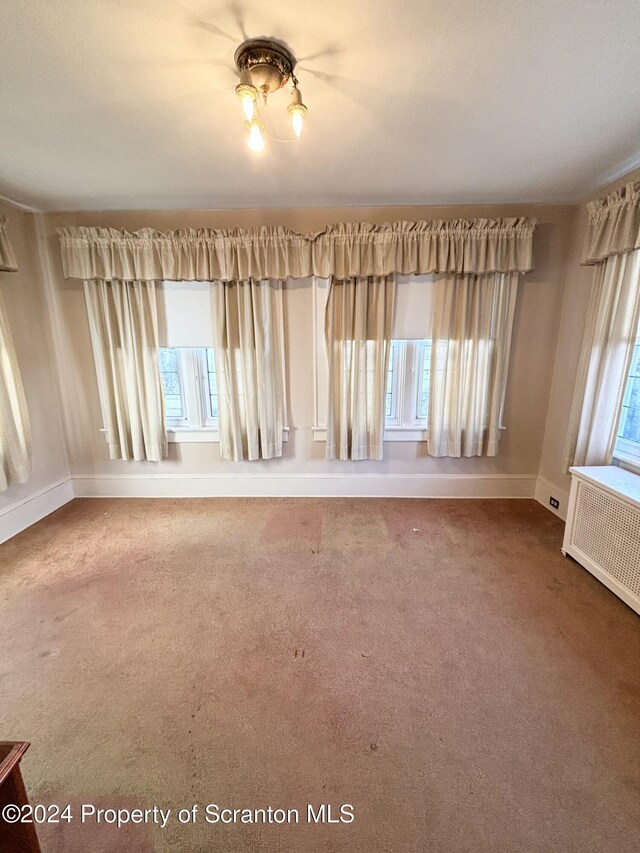 unfurnished room featuring radiator heating unit, carpet, and plenty of natural light