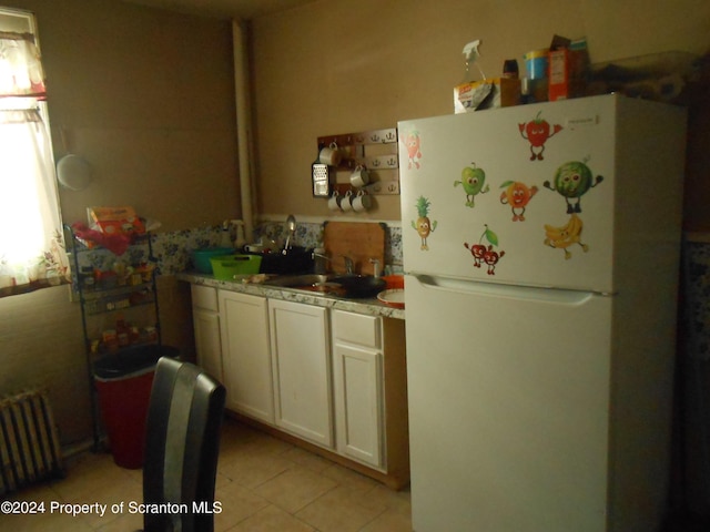 kitchen with radiator, sink, white fridge, white cabinetry, and light tile patterned flooring