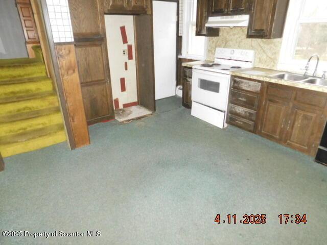 kitchen featuring a sink, light countertops, dark carpet, under cabinet range hood, and white electric range