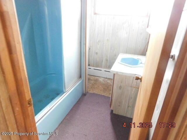 full bath with wooden walls, vanity, and a baseboard radiator