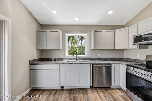 kitchen featuring stainless steel appliances, white cabinetry, a sink, wood finished floors, and baseboards