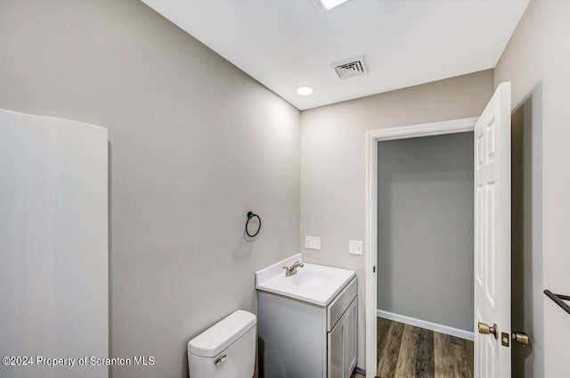 half bath featuring visible vents, vanity, toilet, and wood finished floors