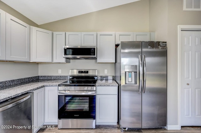 kitchen with vaulted ceiling, appliances with stainless steel finishes, white cabinetry, and light stone countertops