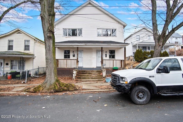 american foursquare style home featuring a porch and fence