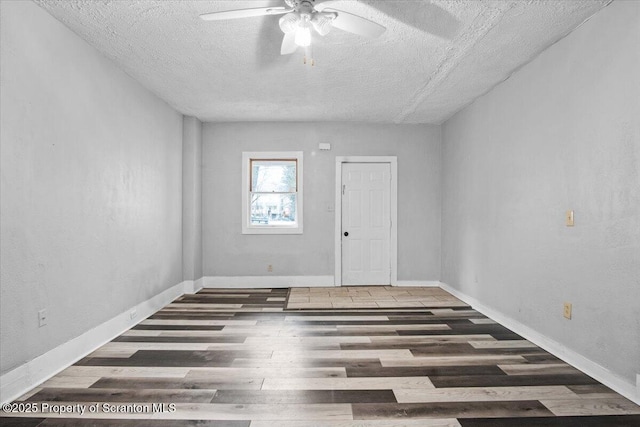 empty room with ceiling fan, a textured ceiling, baseboards, and wood finished floors