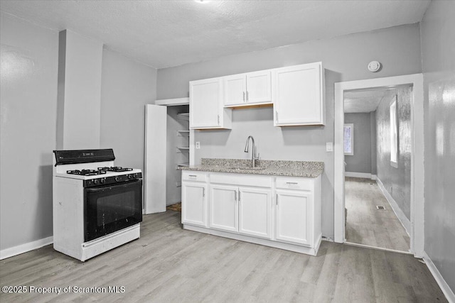 kitchen with light wood finished floors, gas range oven, white cabinetry, a sink, and light stone countertops