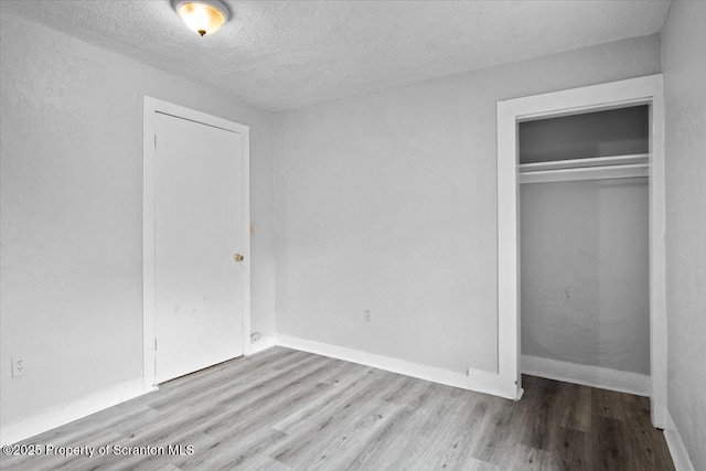 unfurnished bedroom featuring a closet, a textured ceiling, baseboards, and wood finished floors
