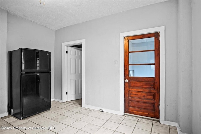 interior space with freestanding refrigerator, light tile patterned flooring, a textured ceiling, and baseboards