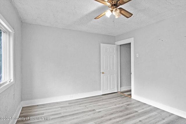 empty room featuring ceiling fan, a textured ceiling, baseboards, and wood finished floors