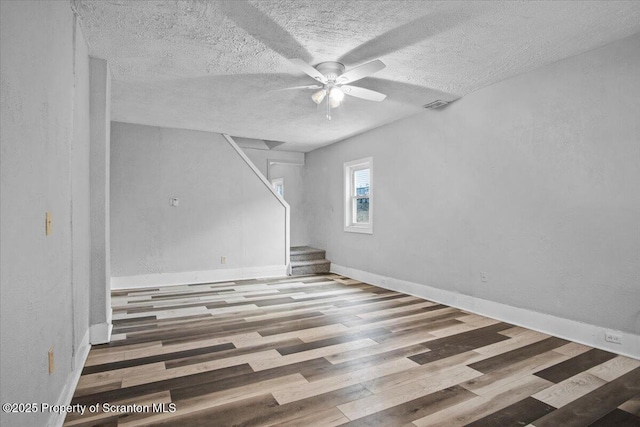 unfurnished room featuring stairs, a textured ceiling, wood finished floors, and a ceiling fan