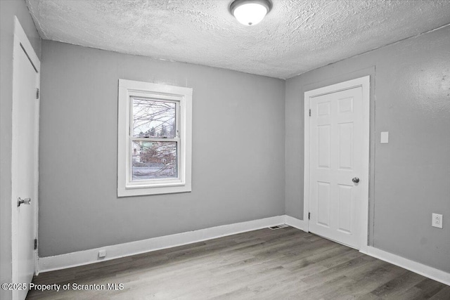 unfurnished room with a textured ceiling, baseboards, and wood finished floors