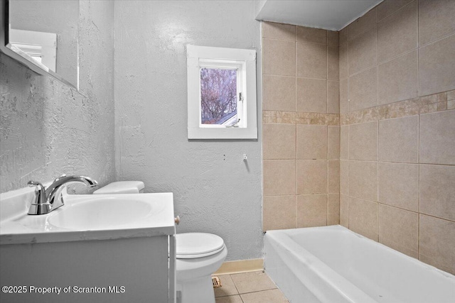 bathroom with a textured wall, toilet, vanity, baseboards, and tile patterned floors
