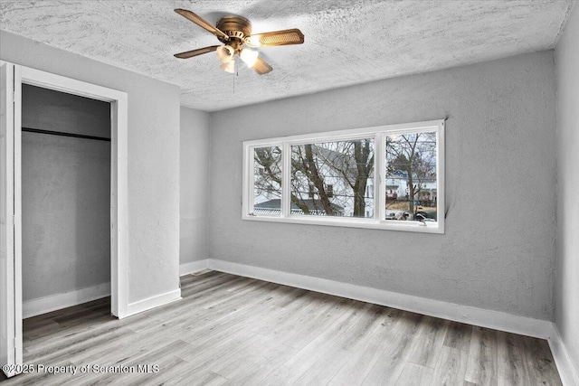 unfurnished bedroom with a textured wall, a textured ceiling, baseboards, and wood finished floors