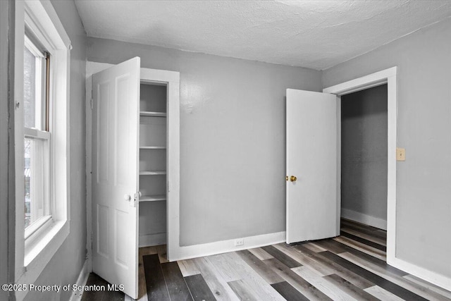 unfurnished bedroom featuring a textured ceiling, baseboards, and wood finished floors