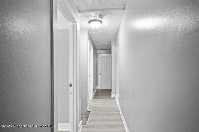 hallway with a textured ceiling, a textured wall, wood finished floors, and baseboards