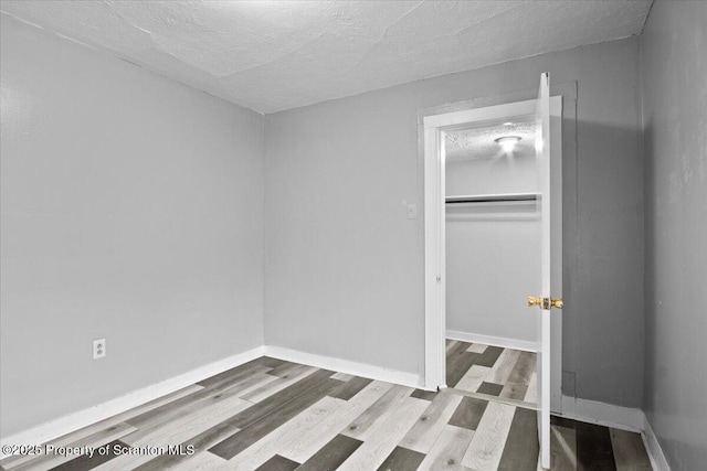 unfurnished bedroom with a closet, a textured ceiling, baseboards, and wood finished floors
