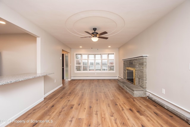 unfurnished living room featuring light hardwood / wood-style flooring, a stone fireplace, ceiling fan, and a baseboard heating unit