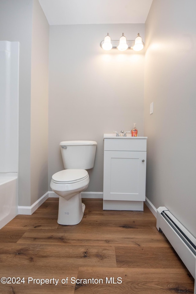 bathroom featuring hardwood / wood-style flooring, toilet, a bathtub, and a baseboard heating unit