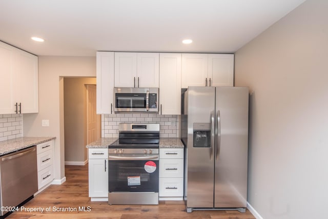 kitchen with hardwood / wood-style floors, decorative backsplash, light stone countertops, appliances with stainless steel finishes, and white cabinetry