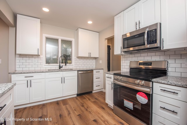 kitchen with appliances with stainless steel finishes, backsplash, sink, light hardwood / wood-style floors, and white cabinetry