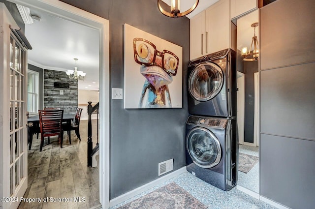 clothes washing area with french doors, stacked washer / dryer, crown molding, a chandelier, and light wood-type flooring