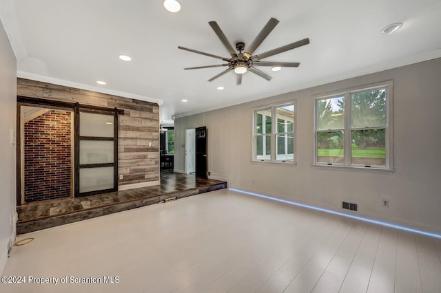 unfurnished living room with ceiling fan, a barn door, and crown molding