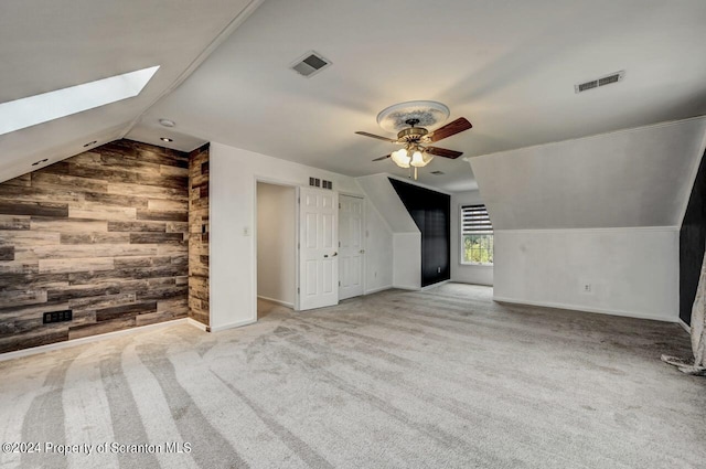 additional living space featuring vaulted ceiling with skylight, light colored carpet, ceiling fan, and wood walls