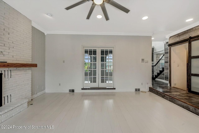 unfurnished living room with crown molding, ceiling fan, a barn door, light wood-type flooring, and brick wall